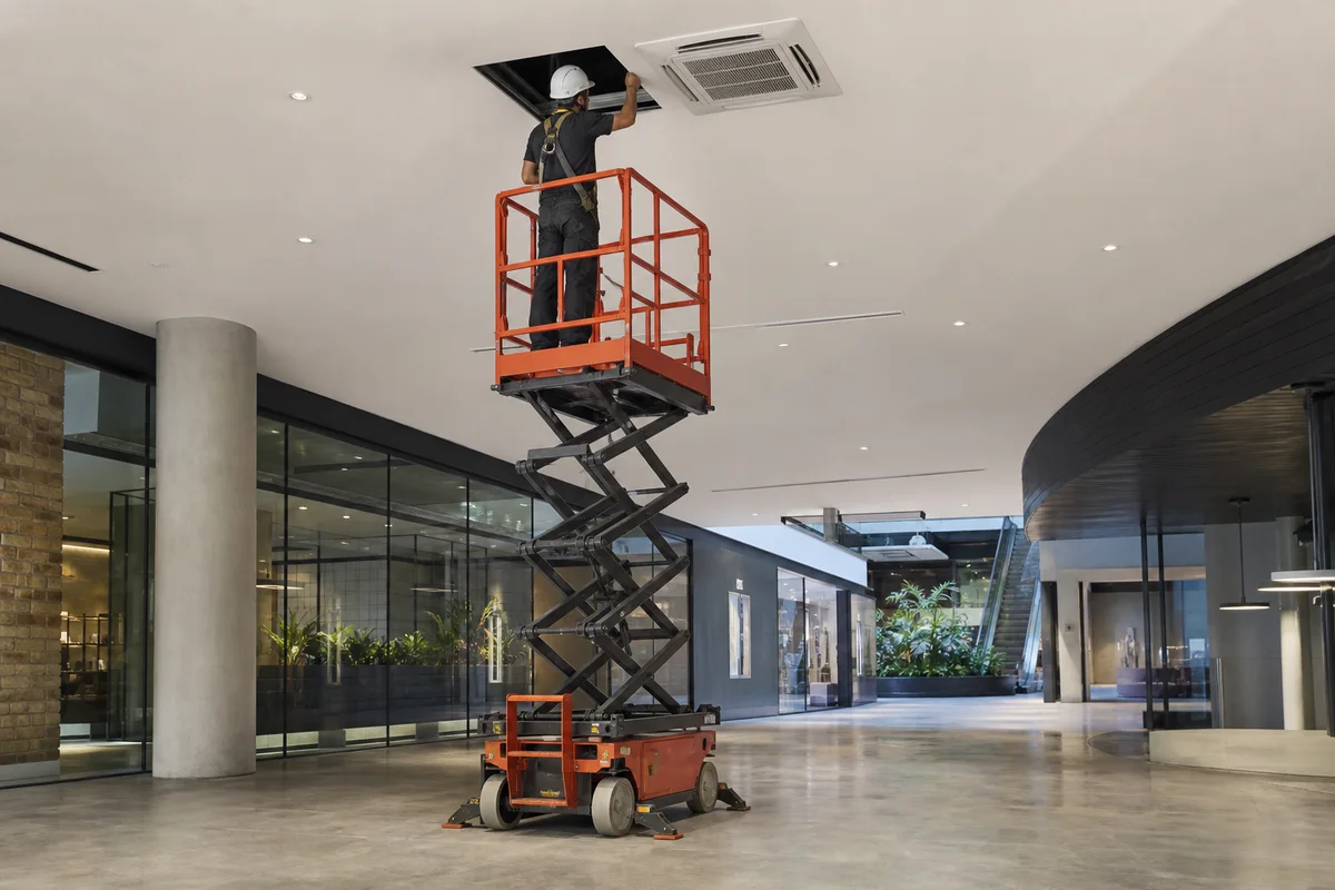 Compact scissor lift raised beneath a high commercial ceiling aircon service point